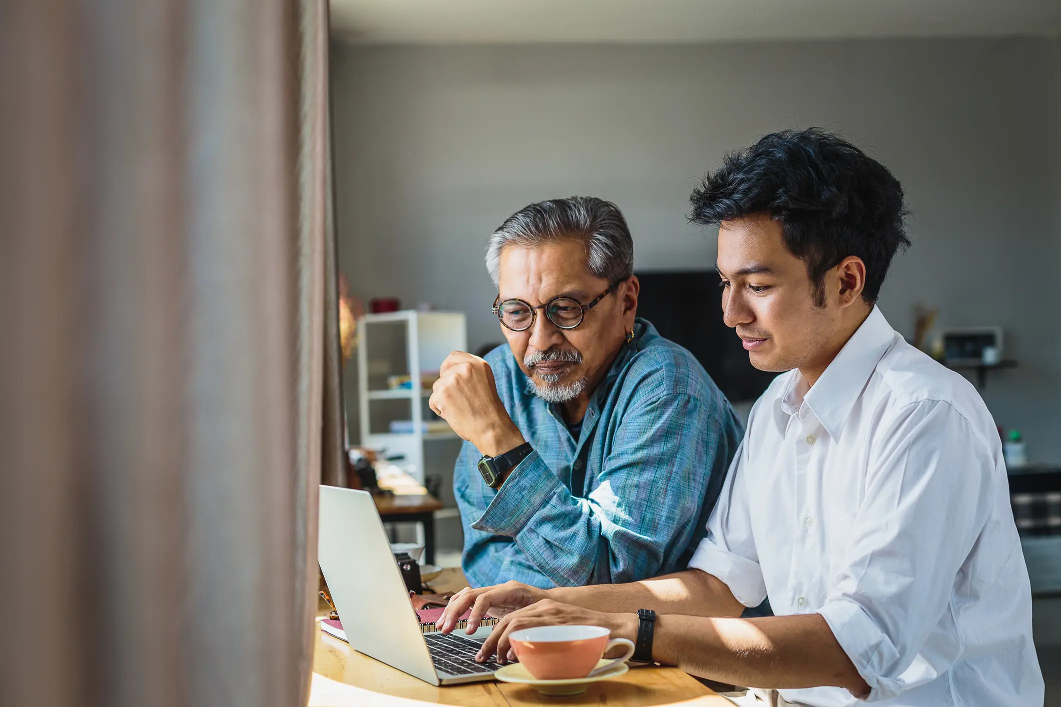 asian senior father and his adult son using laptop computer while sitting at home