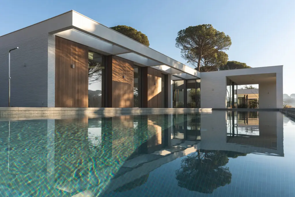 modern white and wood house with pool and pine trees outside