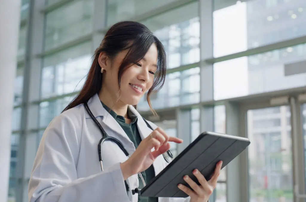 asian woman, doctor and happy in hospital with tablet for prescriptions, research and results. female person, digital and smile for healthcare with appointment, work and wellness in medical career